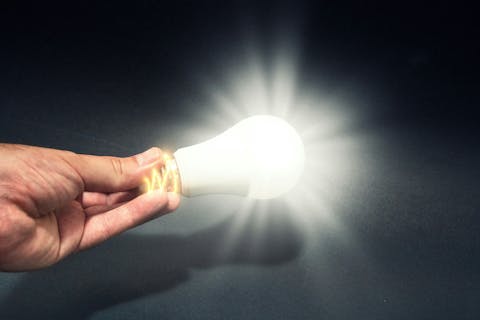 Eine hand hält eine leuchtende Glühbirne